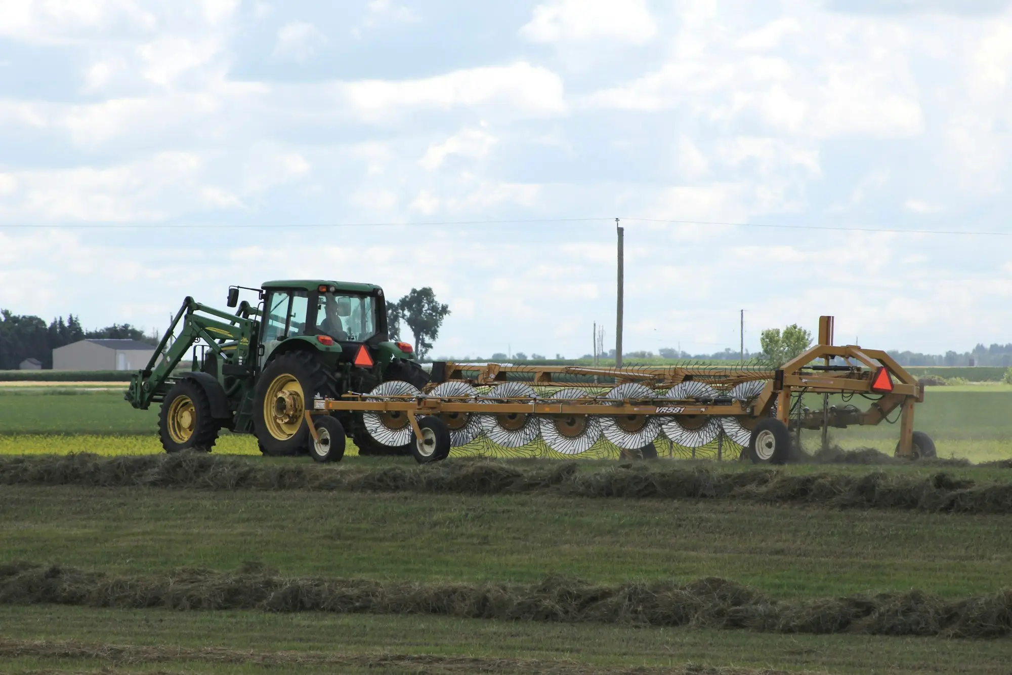 Green tractor with a hay rake working a paddock, the kind of equipment lenders register on the PPSR